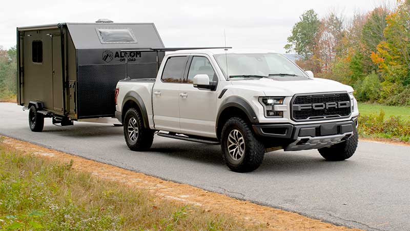 An ALCOM Offroad Caldera overland camper being towed down a country road in the autumn by a Ford F-150.