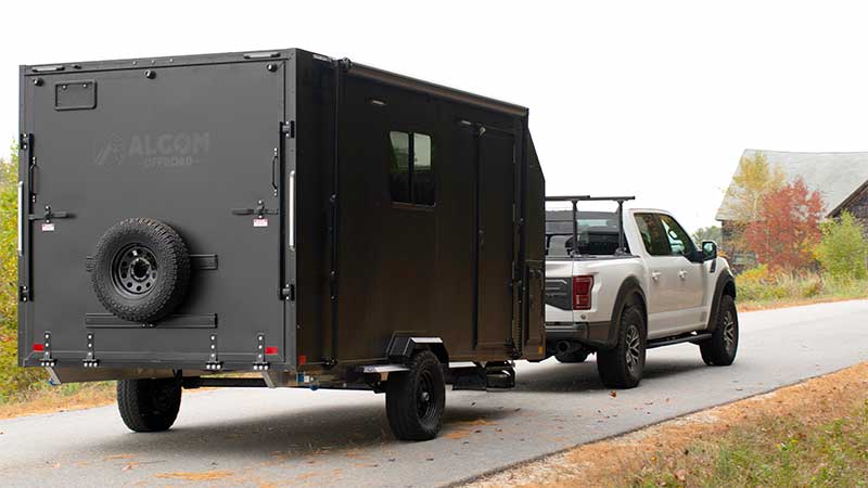 An ALCOM Offroad Caldera overland camper being towed down a country road in the autumn by a Ford F-150. Picture taken from the rear of the trailer.