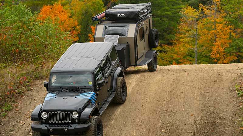 An ALCOM Offroad Oxbow overland camper being towed by a Jeep over a hilly dirt road.