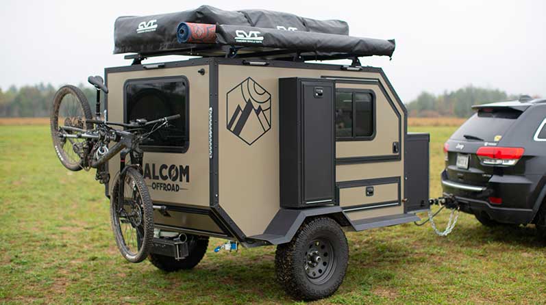 An ALCOM Offroad Oxbow overland camper parked in a field behind a Jeep Grand Cherokee.