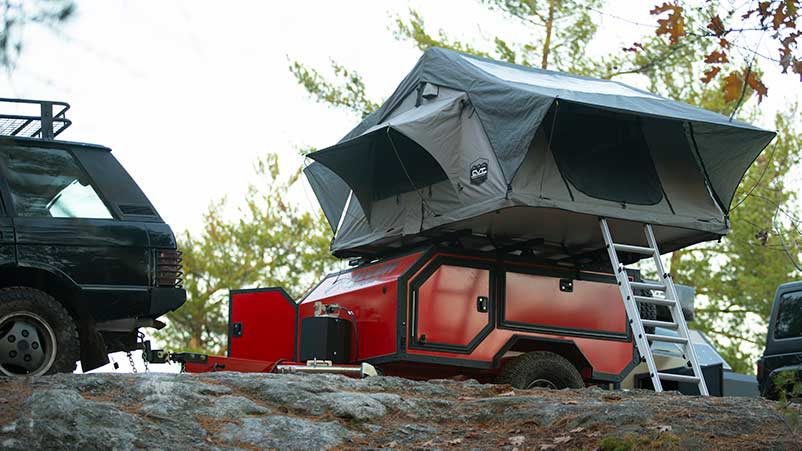 An ALCOM Offroad overland camper with a ladder to access the fully setup rooftop tent.